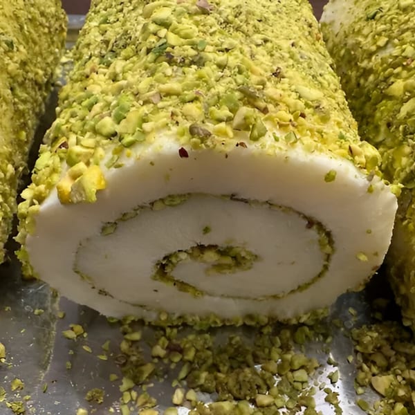 Close-up of a pistachio-dusted Mediterranean dessert roll with a visible spiral filling.