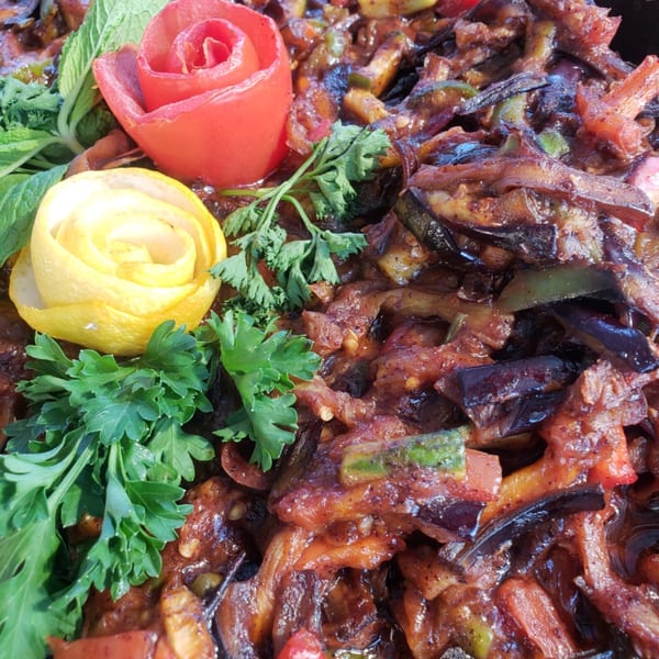 Close-up of Mediterranean eggplant dish with tomato and lemon garnishes, and fresh herbs.