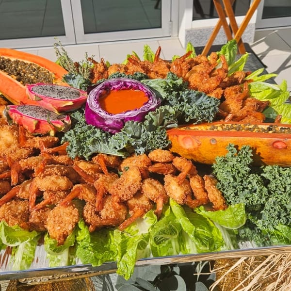 A vibrant platter of fried shrimp, dragon fruit, papaya, and kale with a red cabbage dip.