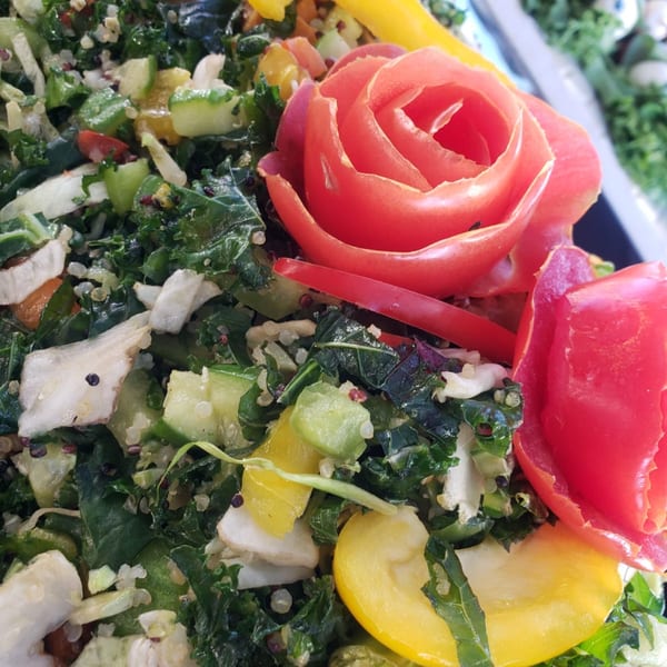 Close-up of a vibrant Mediterranean salad with kale, quinoa, and a tomato carved into a rose.