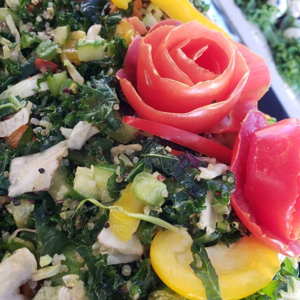 Close-up of a vibrant Mediterranean salad with kale, quinoa, and a tomato carved into a rose.