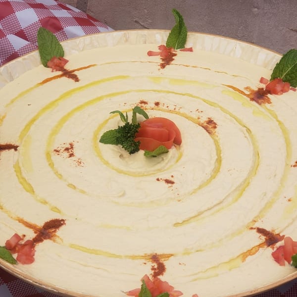 Large platter of Tarbosh Mediterranean hummus, garnished with olive oil, paprika, mint, and tomato.
