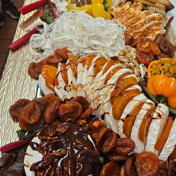 A Mediterranean platter with sliced cheese, dried apricots, walnuts, chicken, and stuffed peppers.