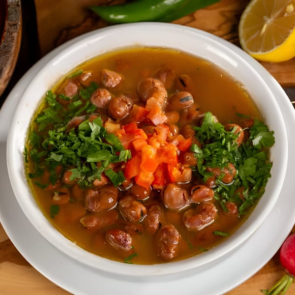 A white bowl of Tarbosh Mediterranean Restaurant's foul mudammas, garnished with diced tomatoes and parsley.