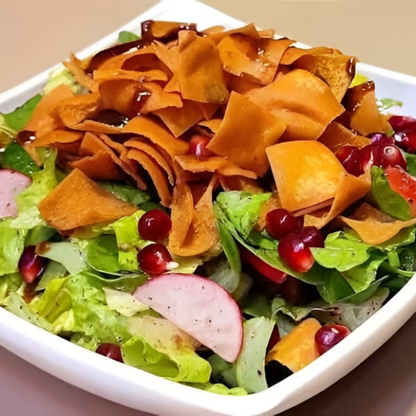 A vibrant Tarbosh Mediterranean salad with crisp lettuce, pomegranate seeds, radishes, and pita chips.