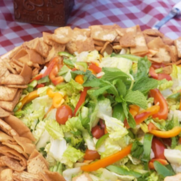 A vibrant Mediterranean salad with fresh greens, bell peppers, tomatoes, and pita chips.